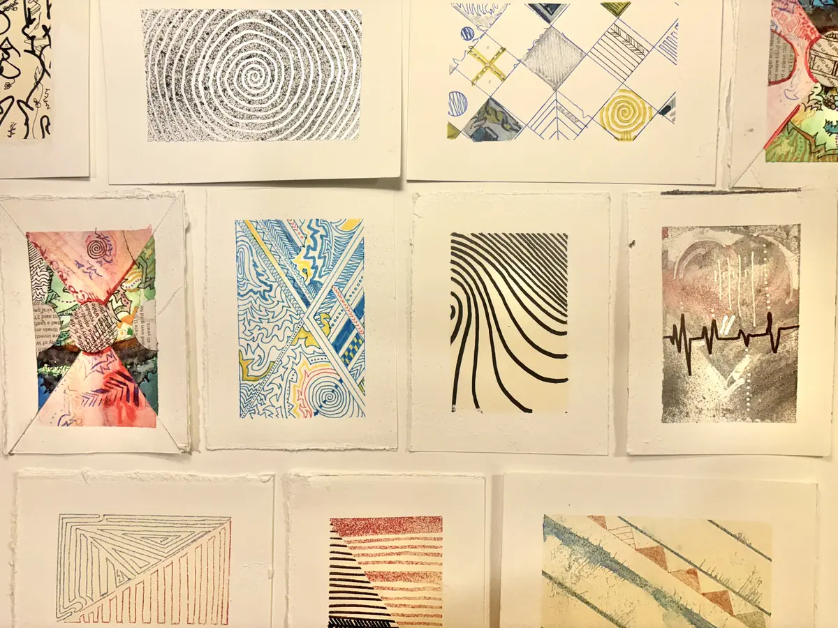A wall of small hand-made cards on deckled paper: ink spirals, watercolour collage, a heart crossed by a heartbeat line, no two alike.
