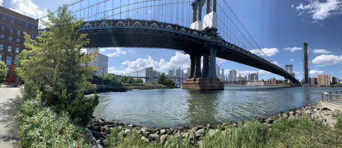 Panorama from the Brooklyn waterfront: the Manhattan Bridge overhead, the Brooklyn Bridge and lower Manhattan beyond it.